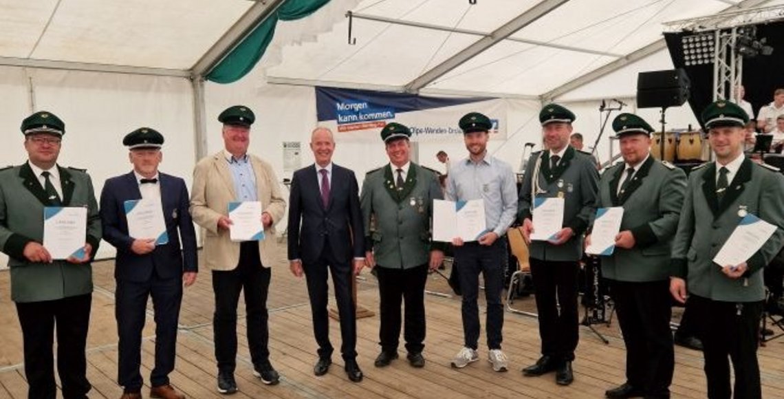 Das Foto zeigt die geehrten Schützenbrüder in grüner Uniform.  Sie stehen im Zelt und haben vom Landrat sowie stellv. Bezirksvorsitzenden Theo Melcher, der in der Bildmitte steht, gerade ihre Urkunde vom Volksbund erhalten.